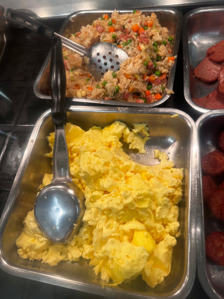 This is a picture showing tray of fried rice, peas, carrots, and spam , along with another tray of fresh eggs.